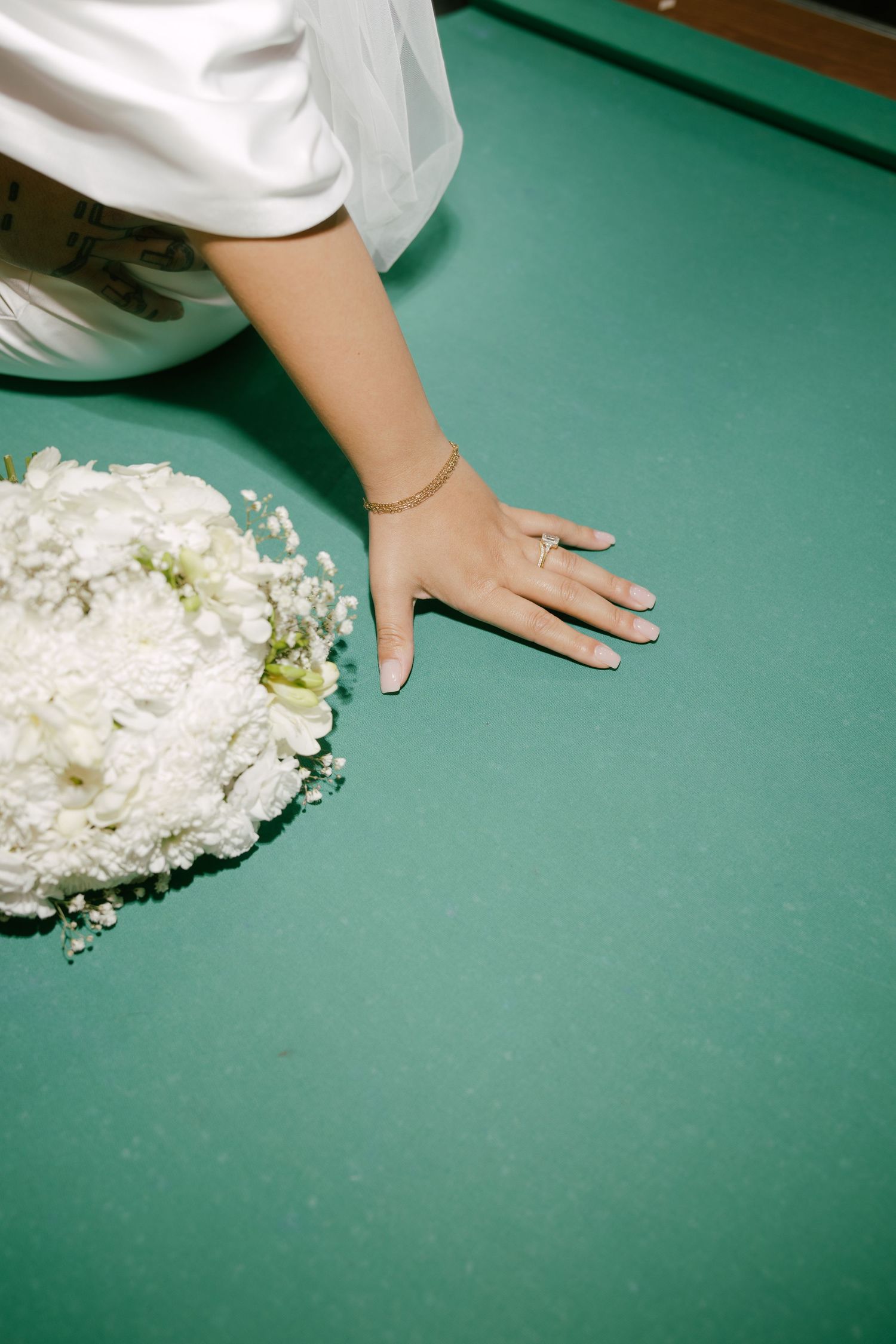 A hand rests on a green surface next to scattered white flower petals and floral arrangements.