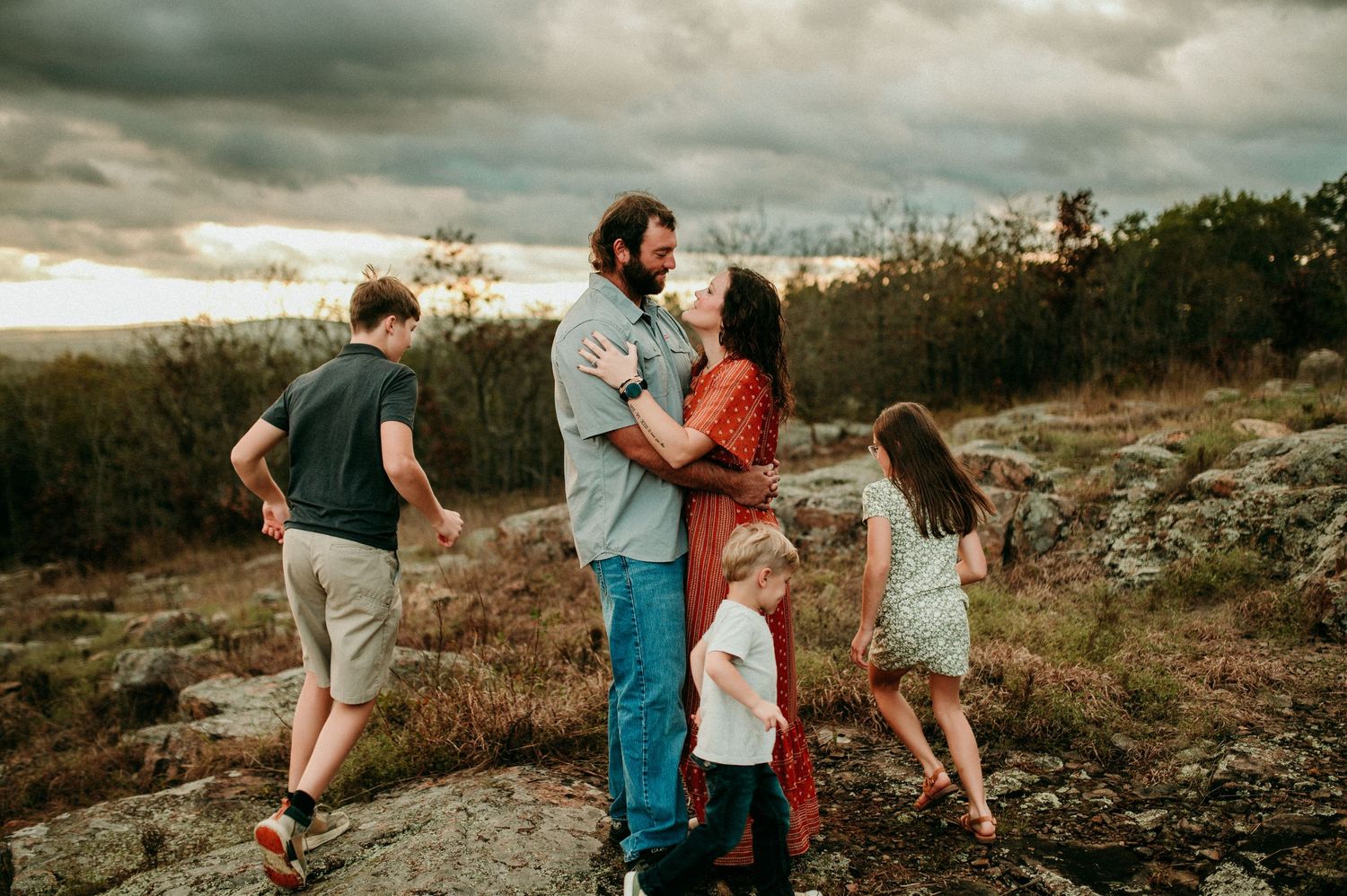 A group of people walking together on a scenic mountain trail during a moody, cloudy sunset.