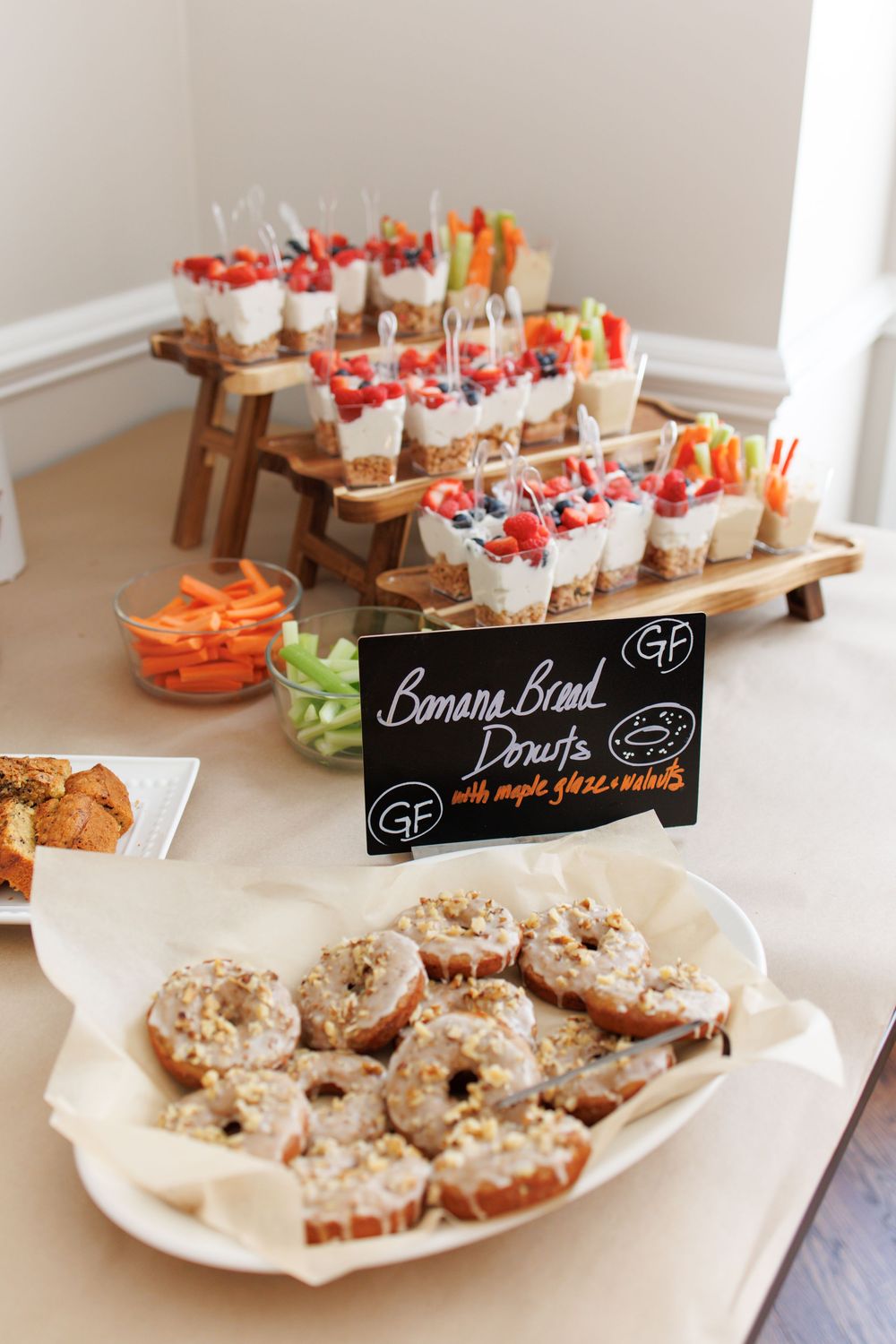 A party food spread featuring banana bread donuts and veggie cups with dip arranged on wooden serving boards.