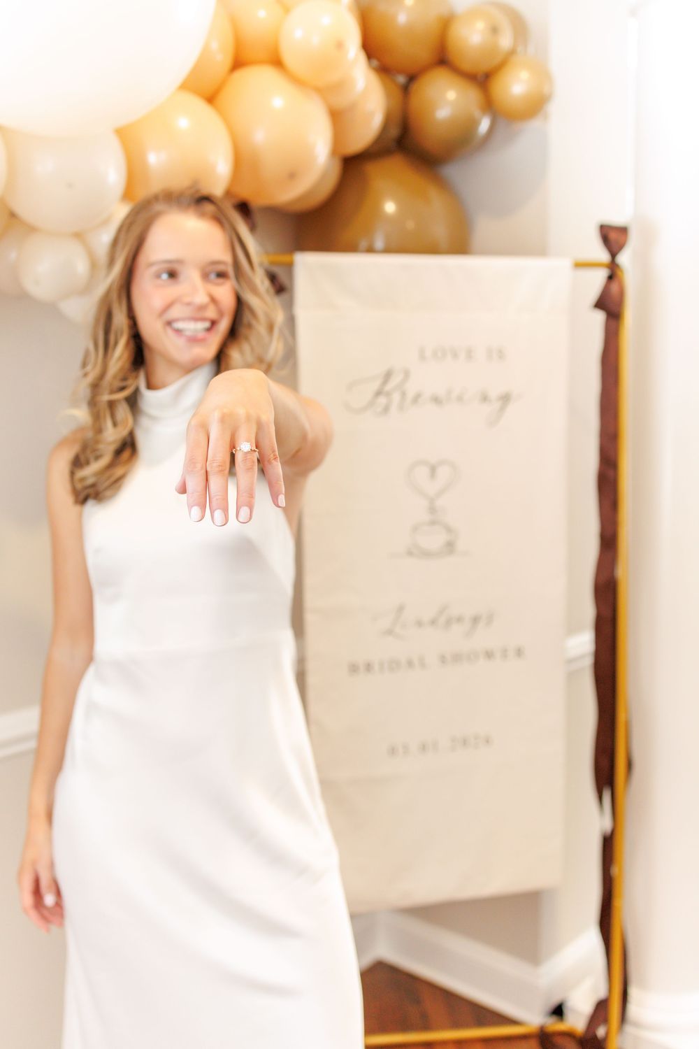 Elegant white decor and gold balloon arrangements for bridal shower with signage and decorative elements.