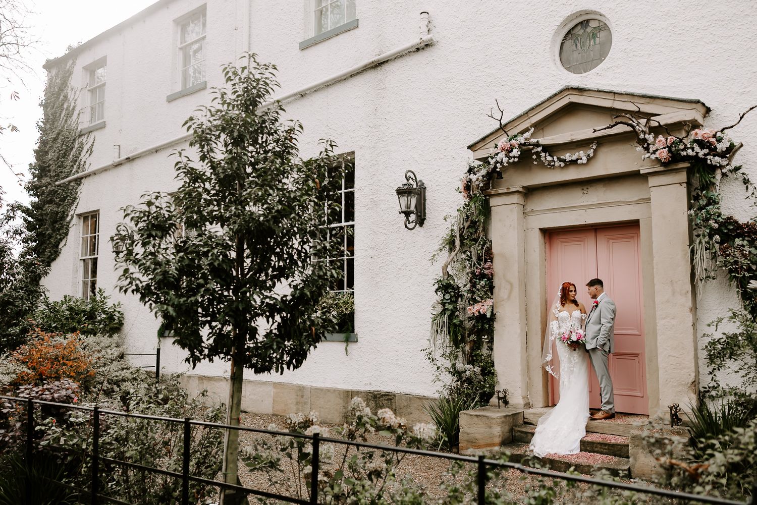 White exterior of a traditional house with multiple arched doorways and windows, surrounded by lush greenery.
