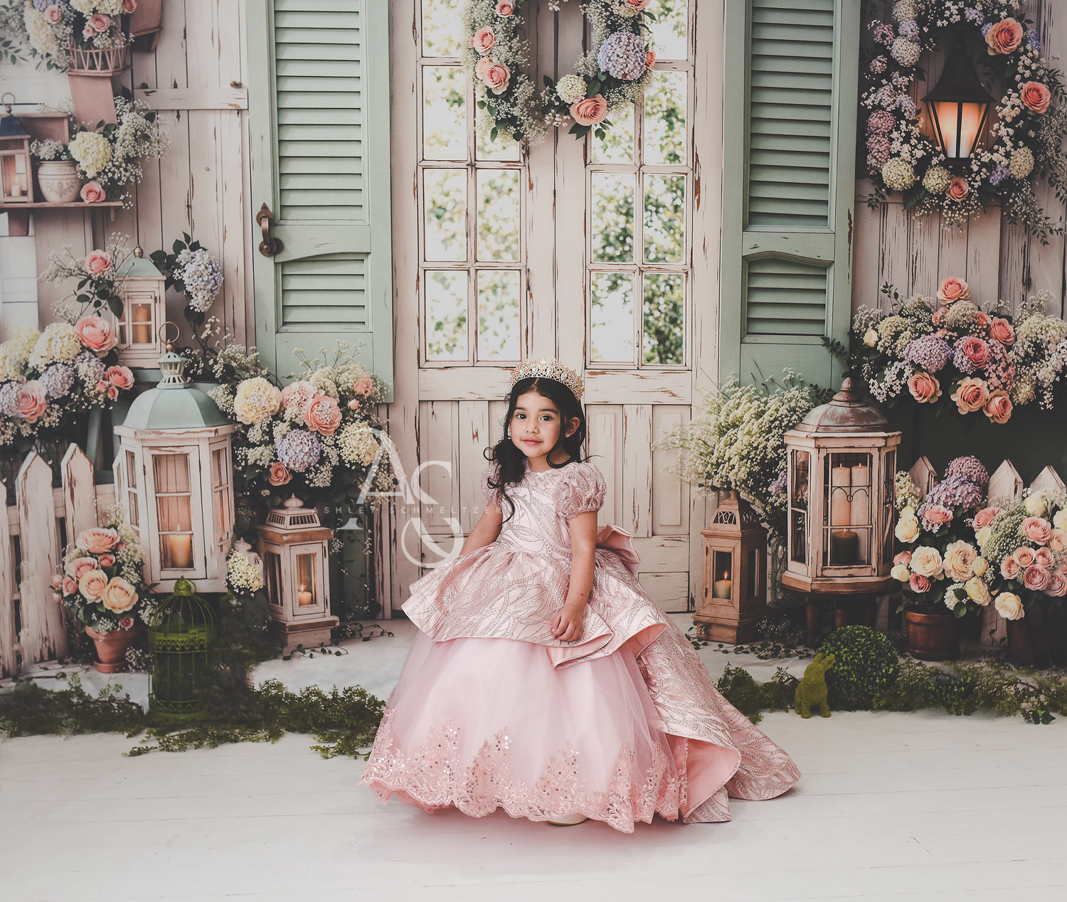 Young girl in elegant pink ball gown posing before floral decorated vintage doors in studio portrait.