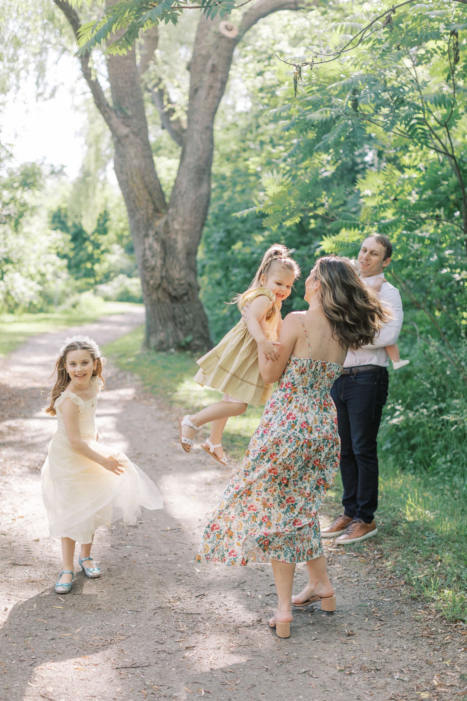 A joyful family moment captured on a sunlit forest path as they dance and twirl together on a summer day.