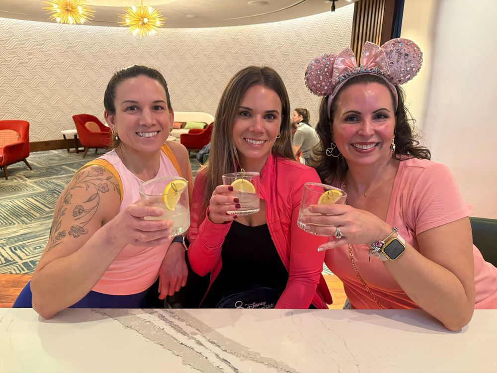 A group of people in pink shirts raise glasses in a celebratory toast at a gathering.