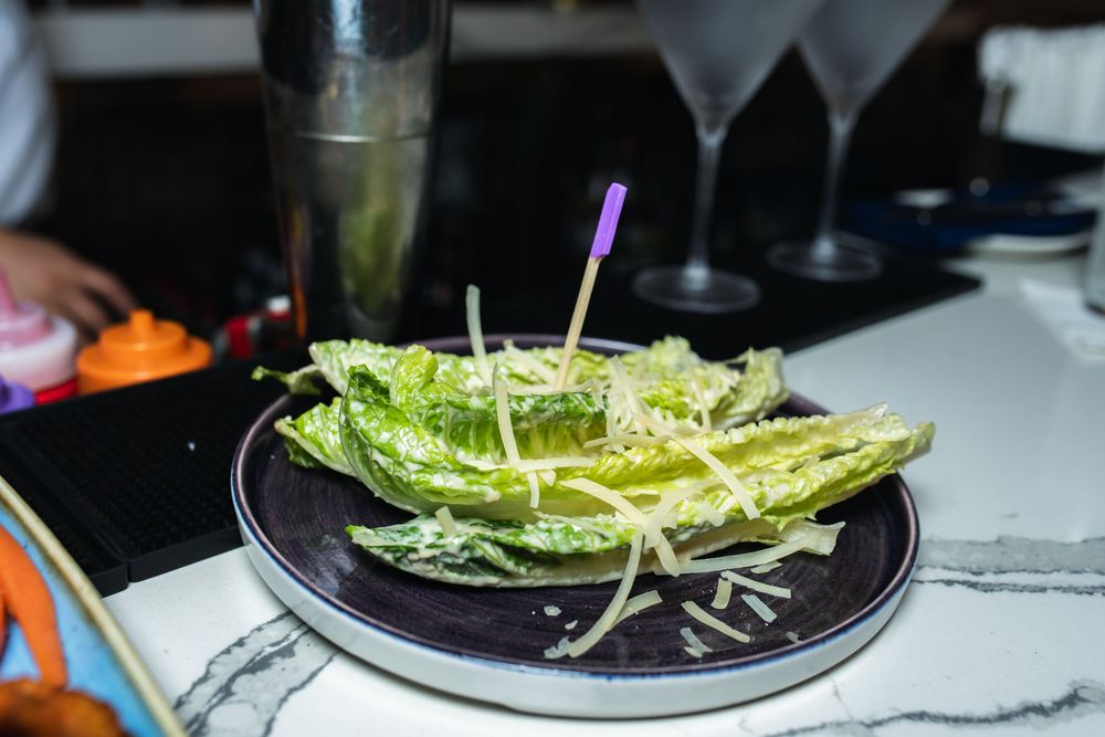 Grilled romaine lettuce hearts with parmesan cheese and dressing drizzle on a black plate.