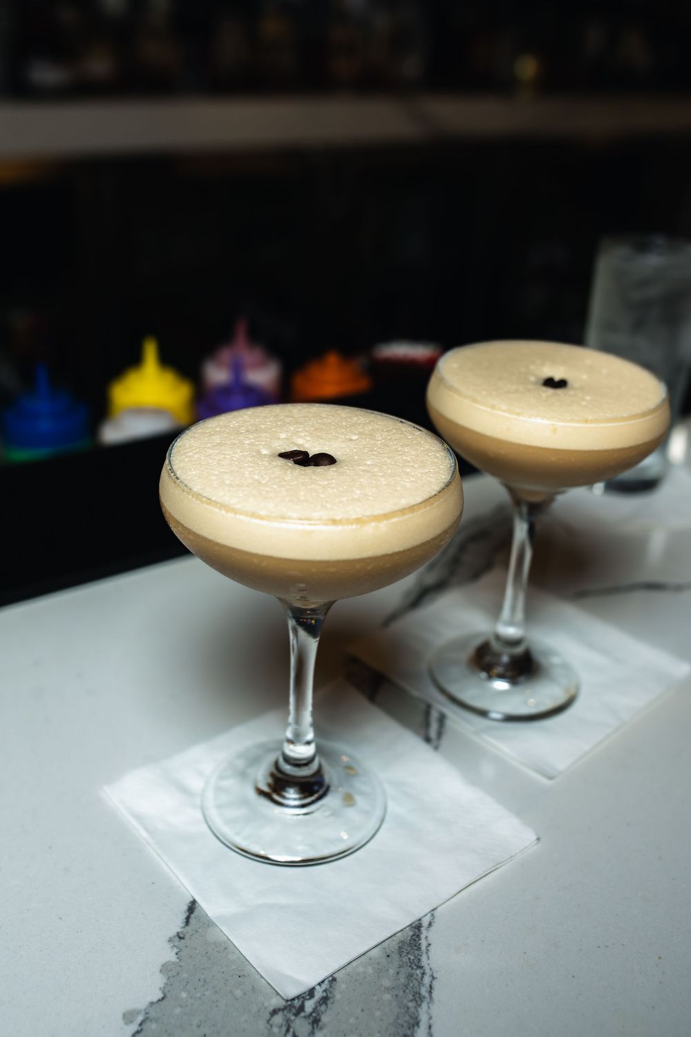 Elegant cocktail served in a coupe glass with a creamy foam top and dark garnish on a white surface.