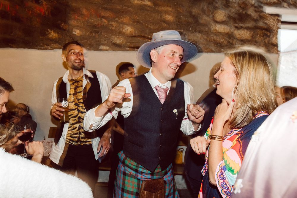 Couples dancing together at a lively party with stone walls and warm lighting in the background.