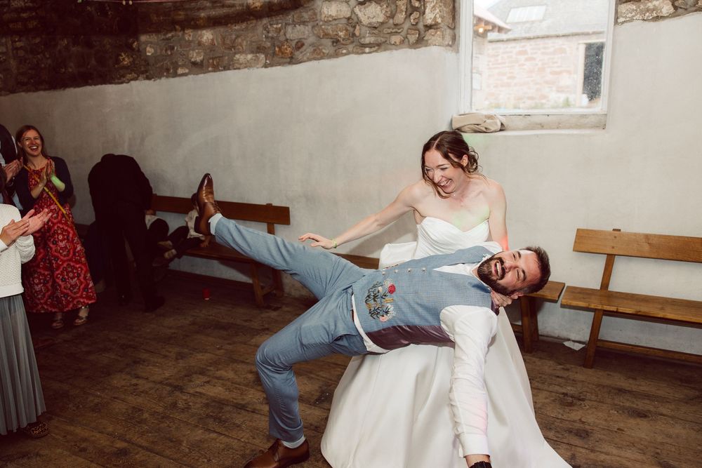 Dancers performing energetic swing dance moves in a rustic indoor venue.