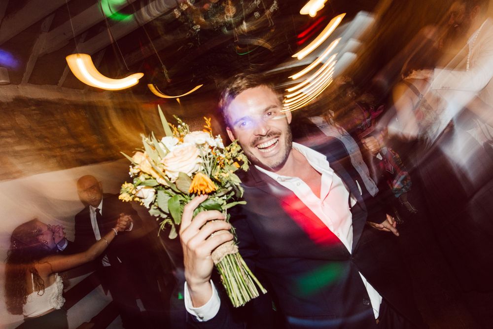 A group of people dancing and celebrating at a dimly lit party venue with colorful lights in the background.