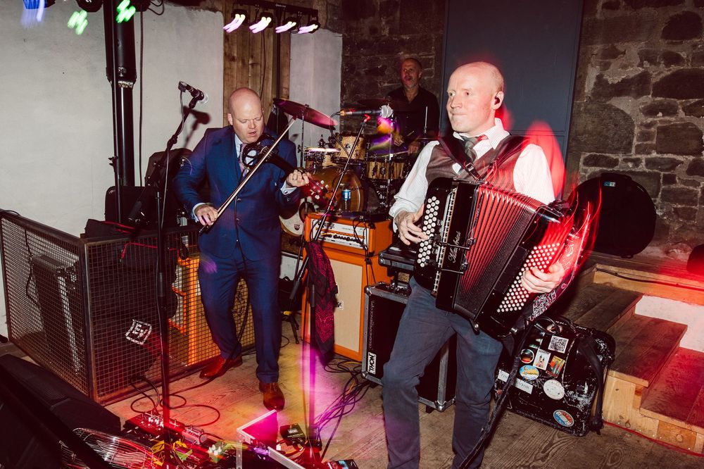 Musicians performing on stage with instruments at a dance event in a stone-walled venue.