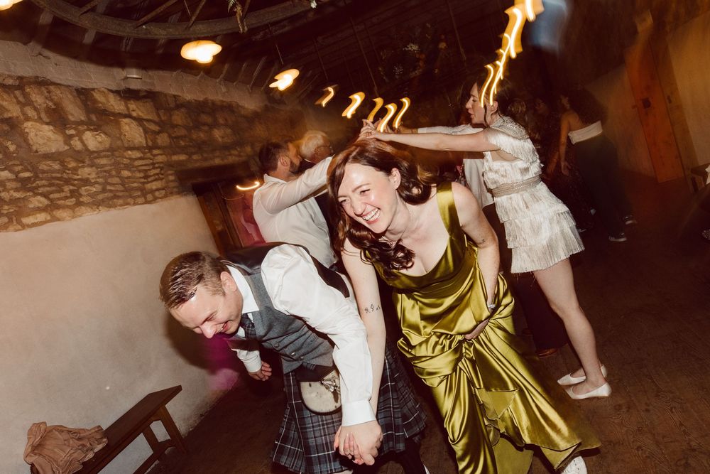Couples dance together in a dimly lit rustic venue during a wedding celebration.