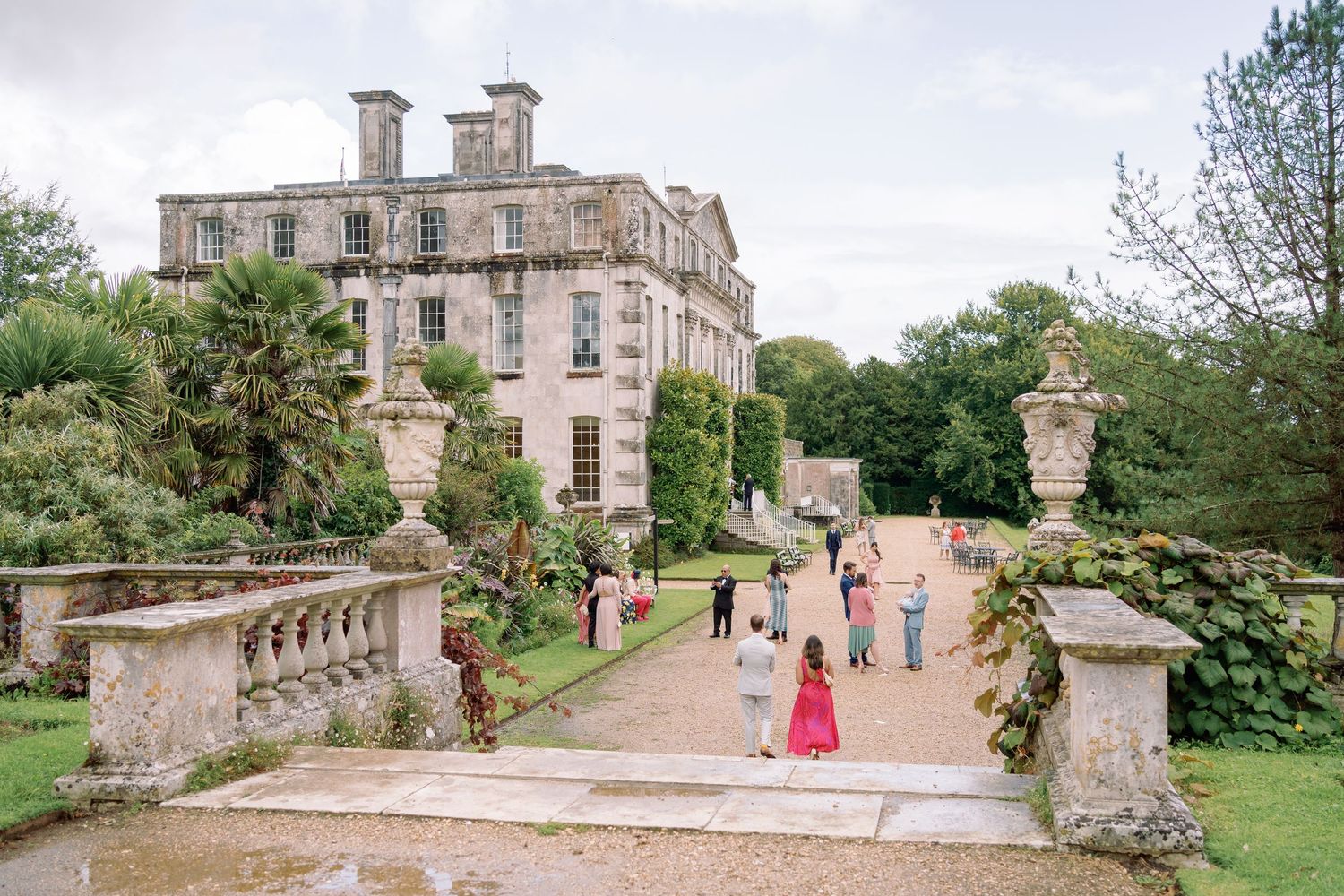 Elegant stone mansion with ornate balustrades and garden paths where visitors stroll on the grounds in summer.