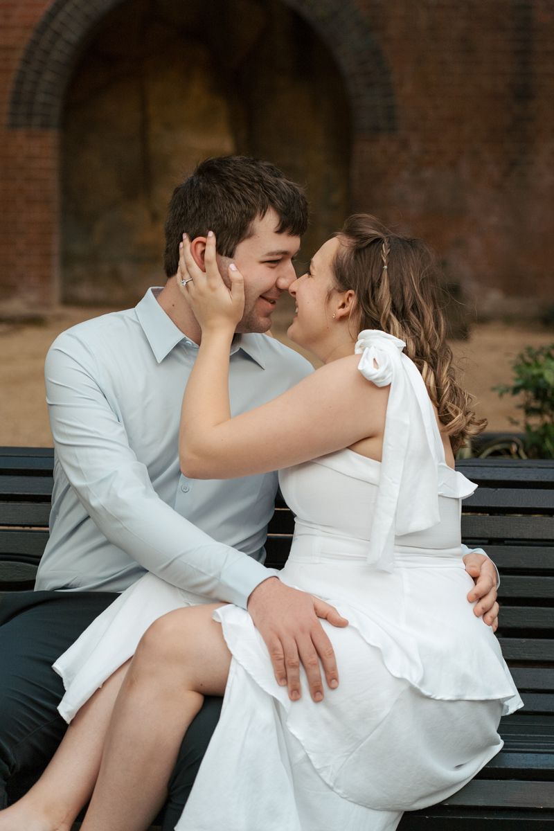 Romantic couple in white clothing sharing intimate moments while sitting together on a park bench at The rocks during an engagement shoot