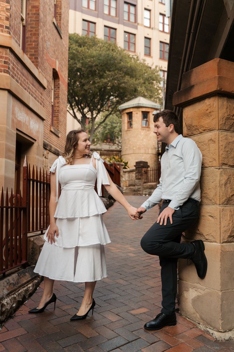 couple in formal attire poses playfully on brick steps outside at buildings in a romantic photo series in the Rocks engagement photoshoot