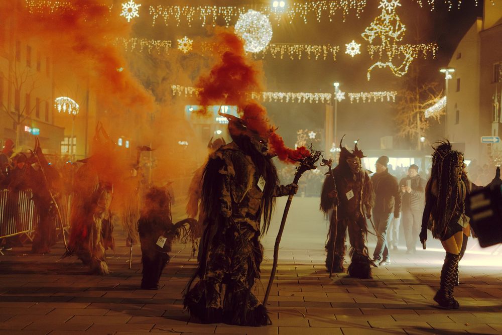 Silhouettes of people walking through a festival with glowing lights and decorations overhead.