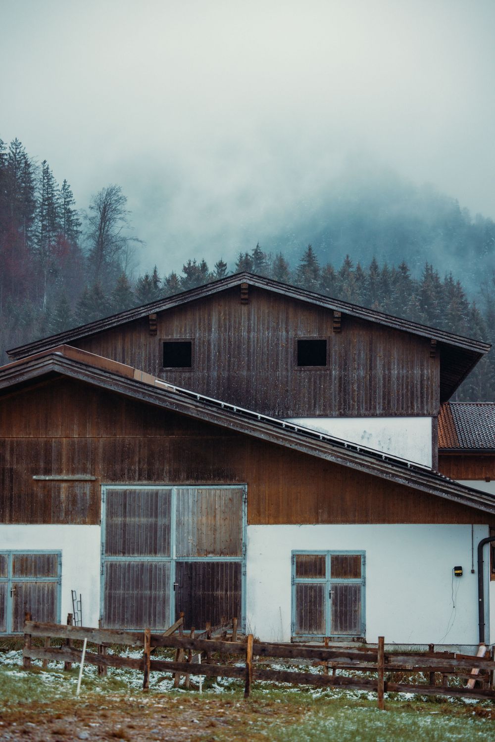 Rustic wooden cabins nestled against a misty mountain backdrop in winter.