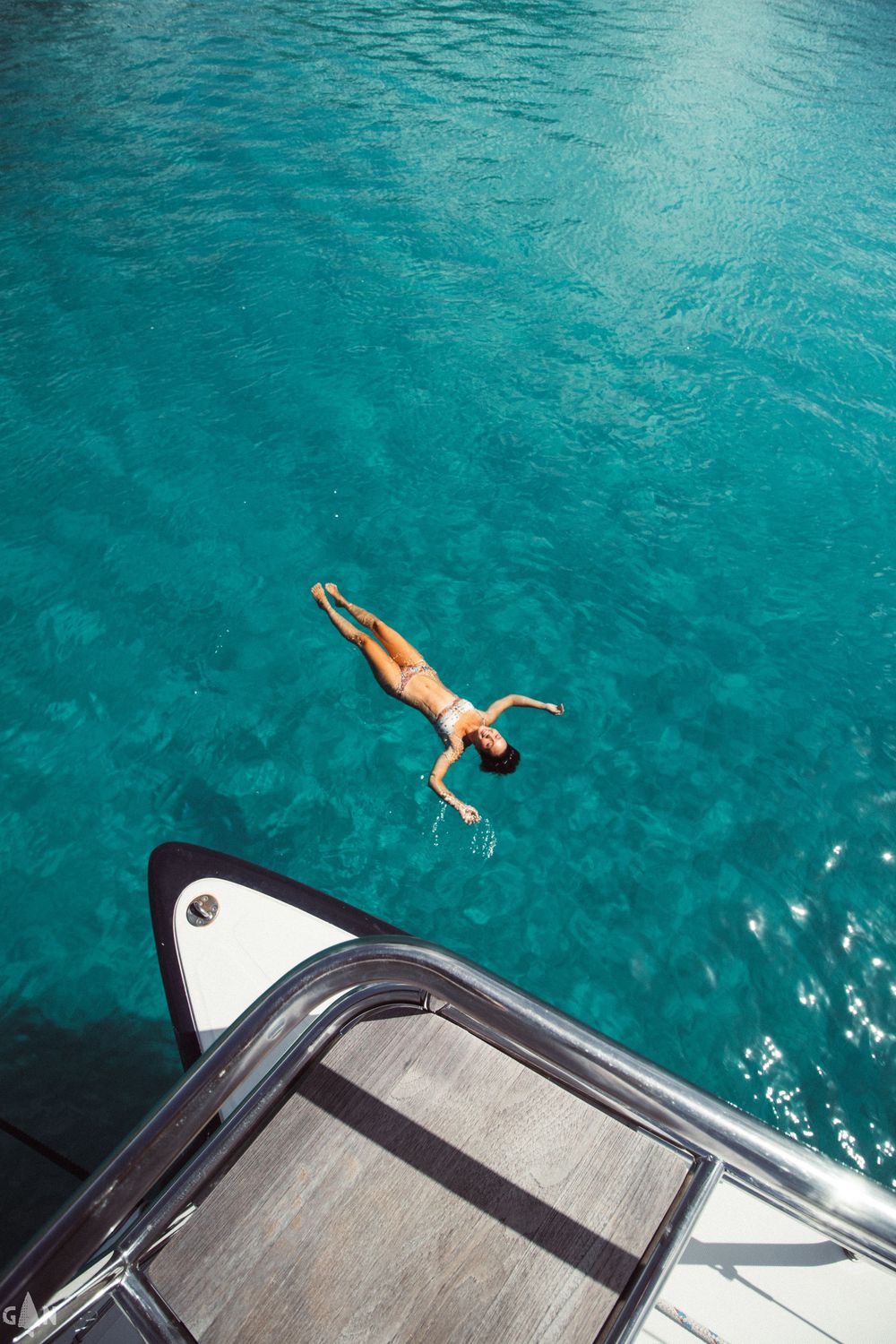 View from boat deck of someone diving into crystal clear turquoise ocean waters.