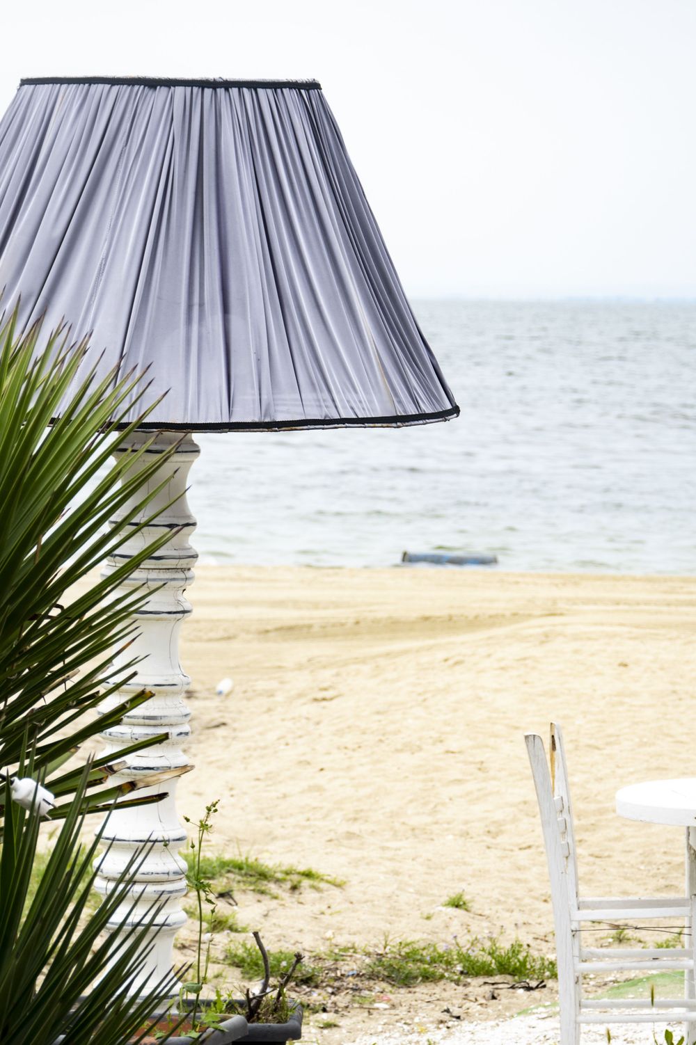 A stylish gray pleated lampshade with palm fronds and sandy beach in the background creates a coastal ambiance.