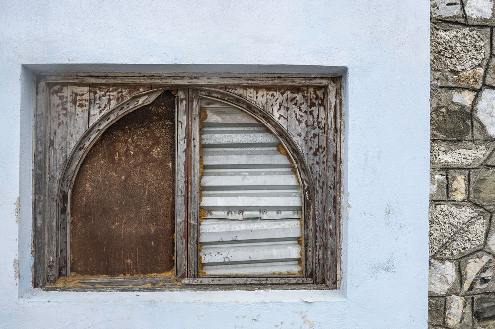 A rustic stone wall with three weathered window frames showing peeling paint and aged wood details.