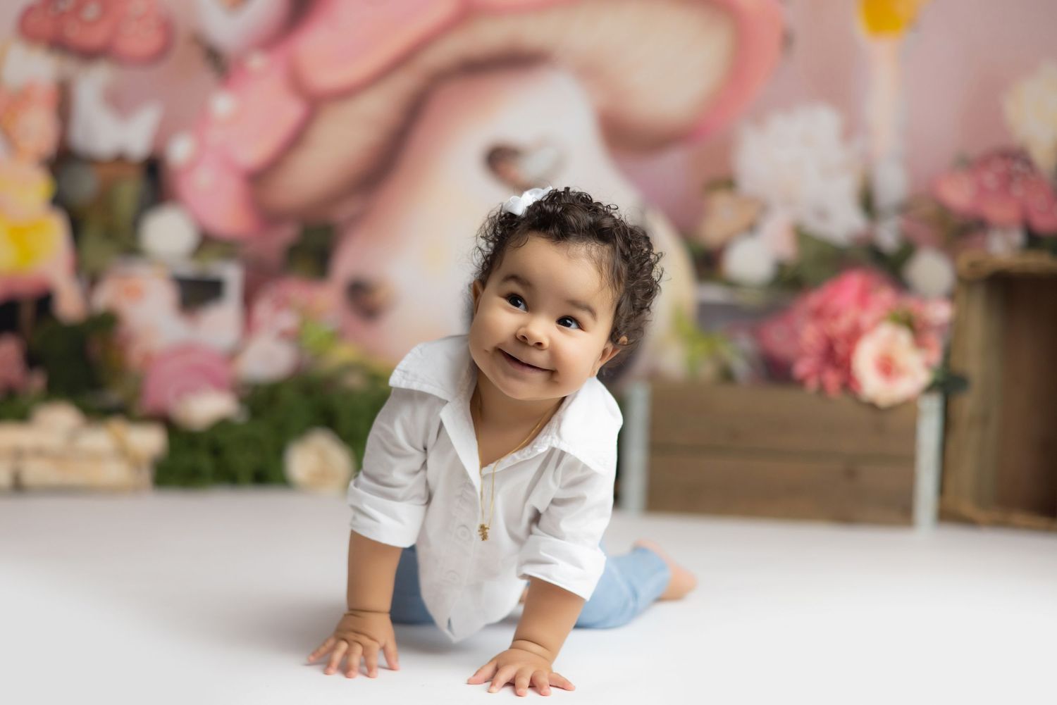 Baby in white shirt crawls and plays on pink floral backdrop during professional photo session.