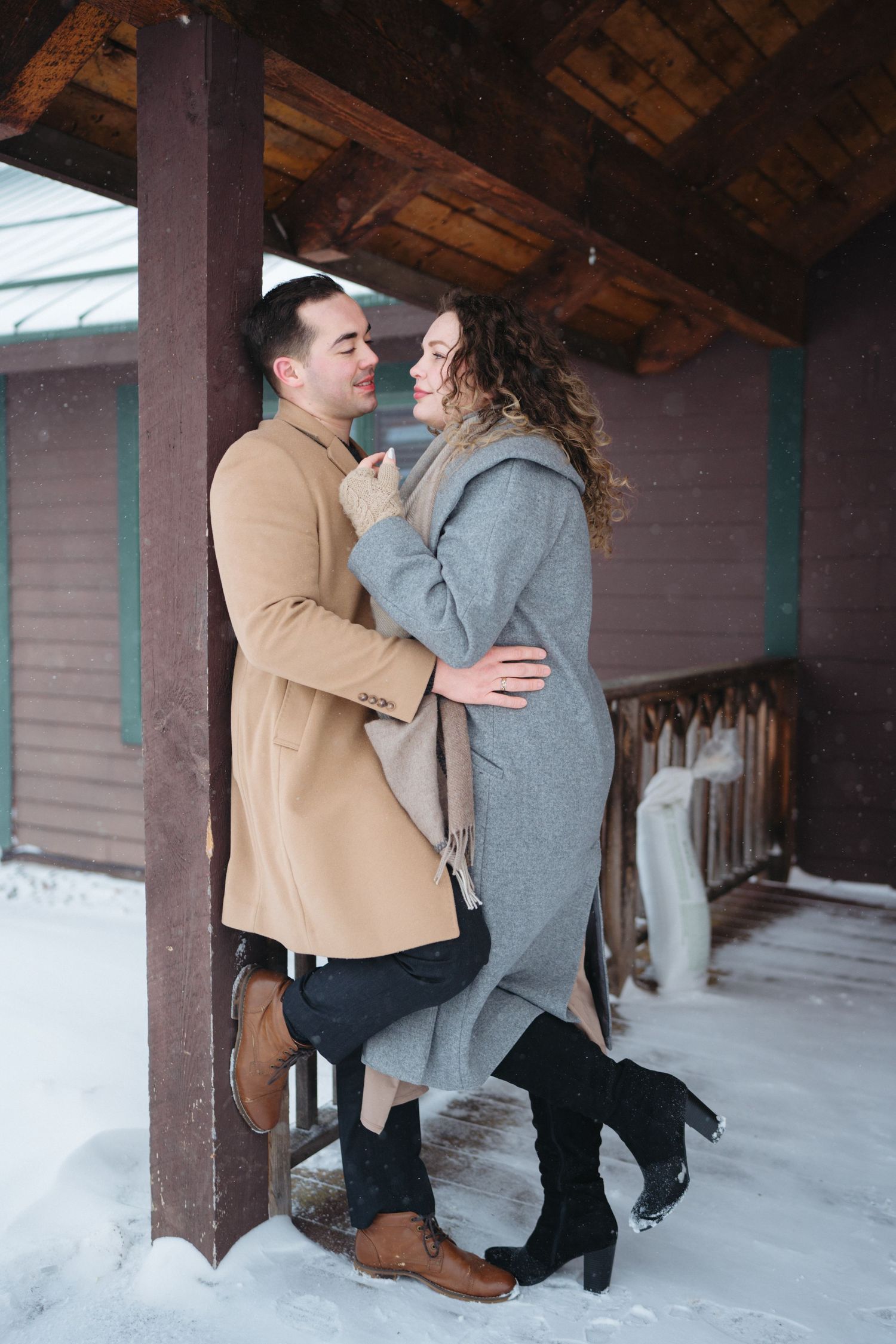 A romantic couple embraces under a rustic wooden porch roof surrounded by snow.