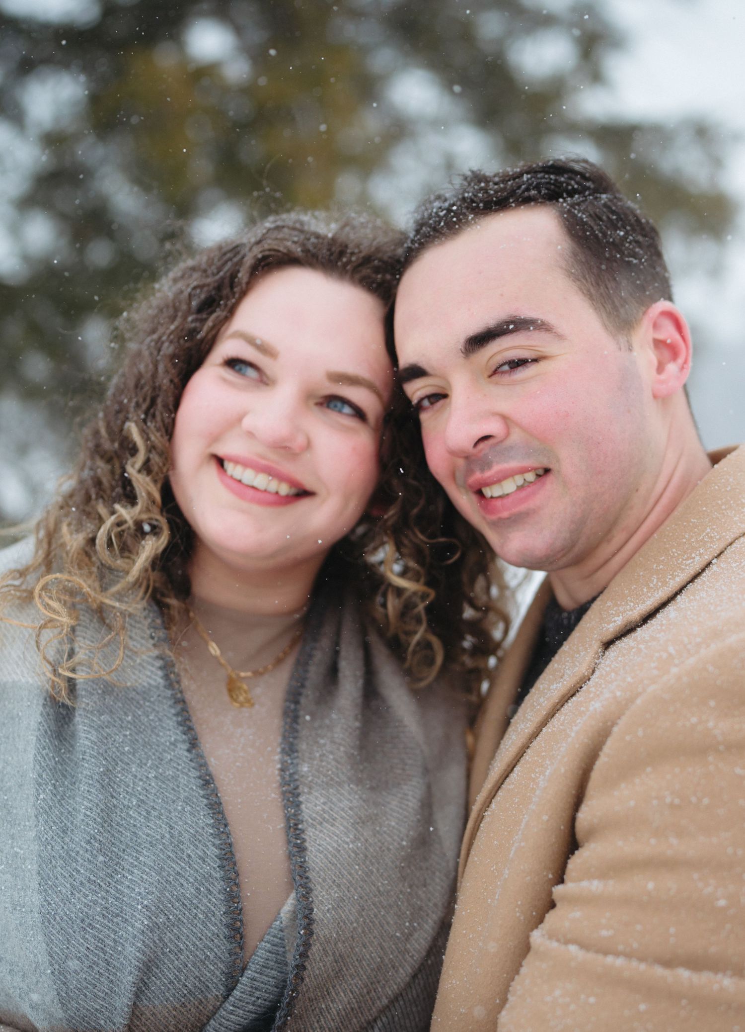 Snowy winter portrait captures a couple in warm coats smiling and embracing outdoors.