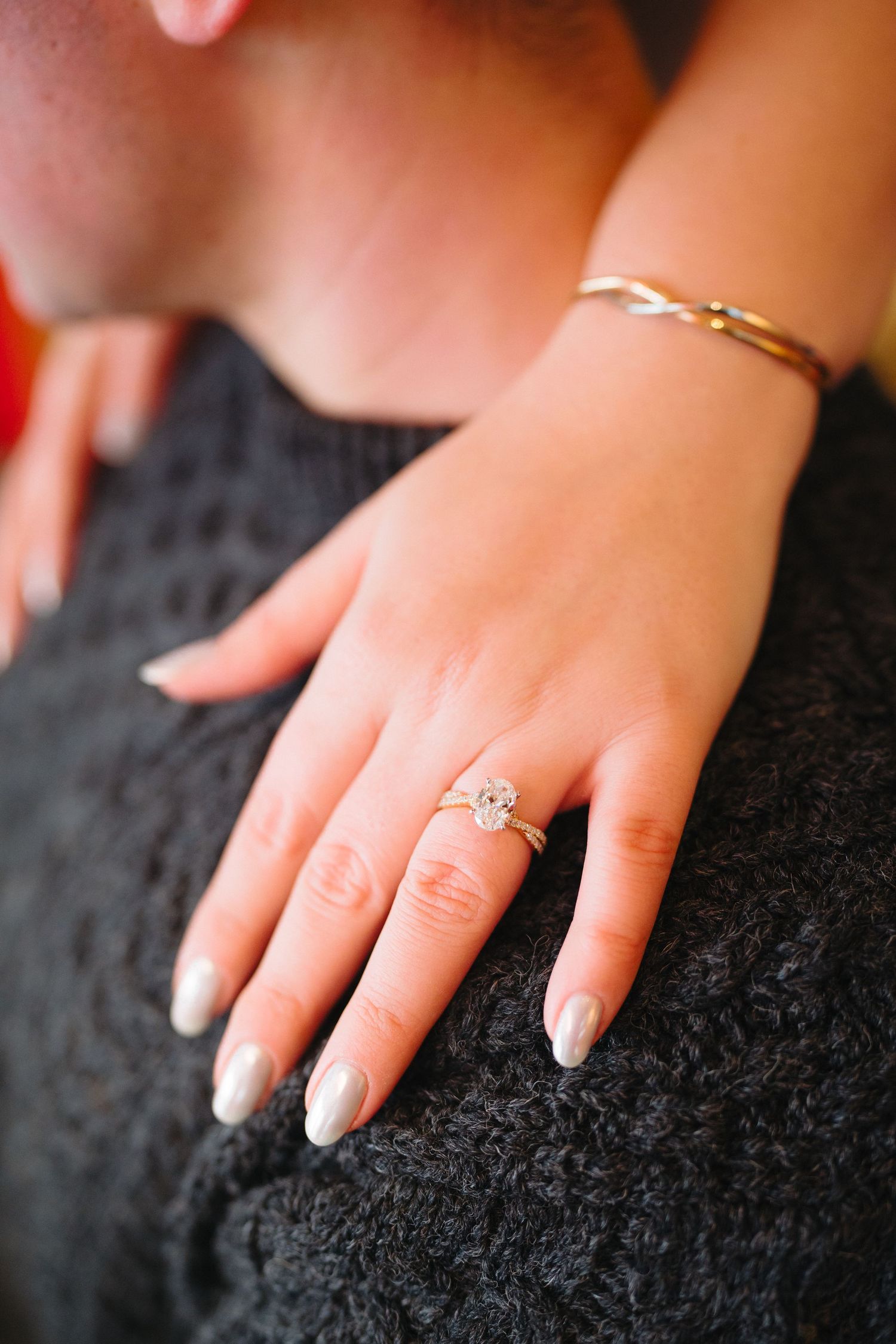 Close-up of hands displaying an elegant diamond engagement ring on a black textured surface.