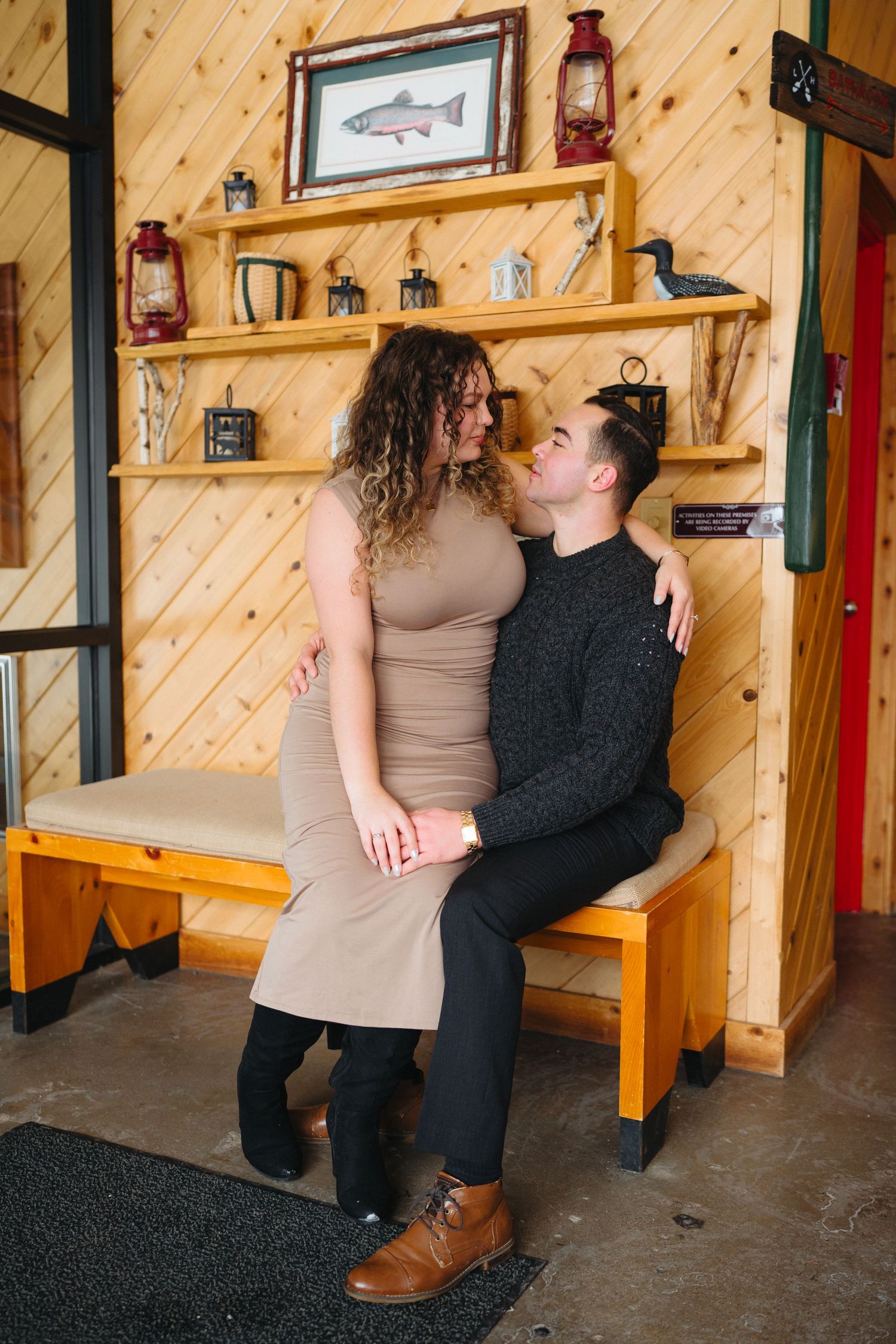 A couple shares an intimate moment on a wooden bench against pine walls decorated with rustic lanterns and fish artwork.