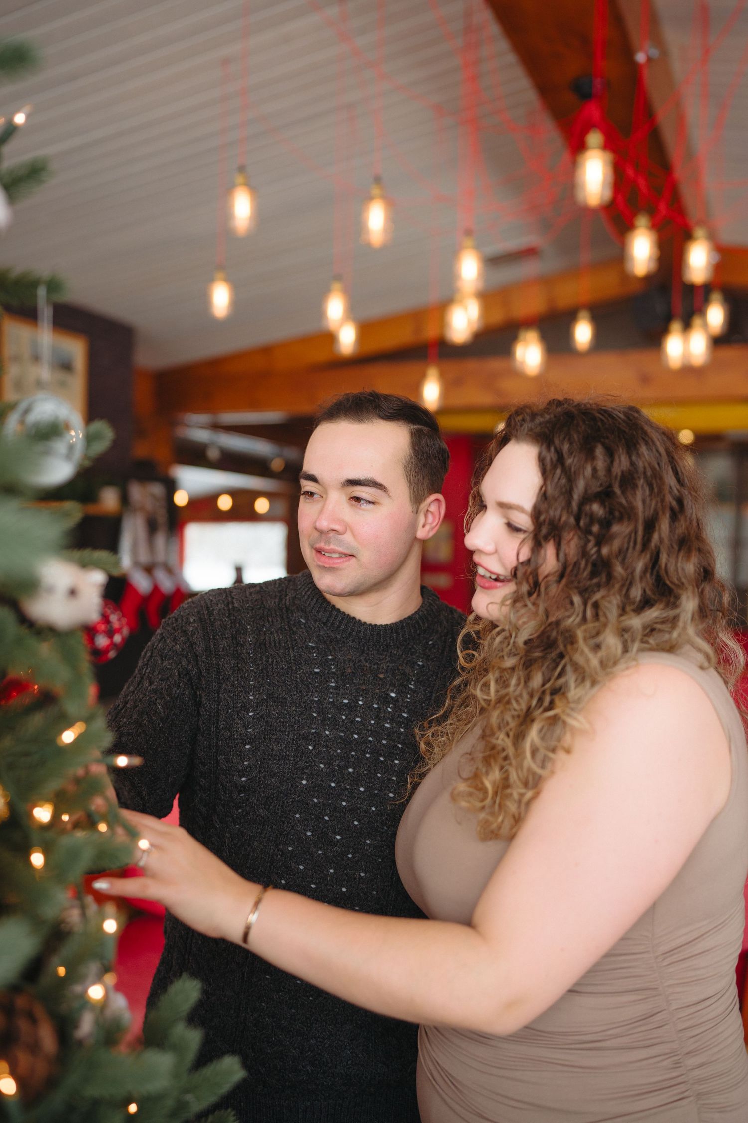 A couple dances together in a room decorated with hanging pendant lights and holiday decorations.