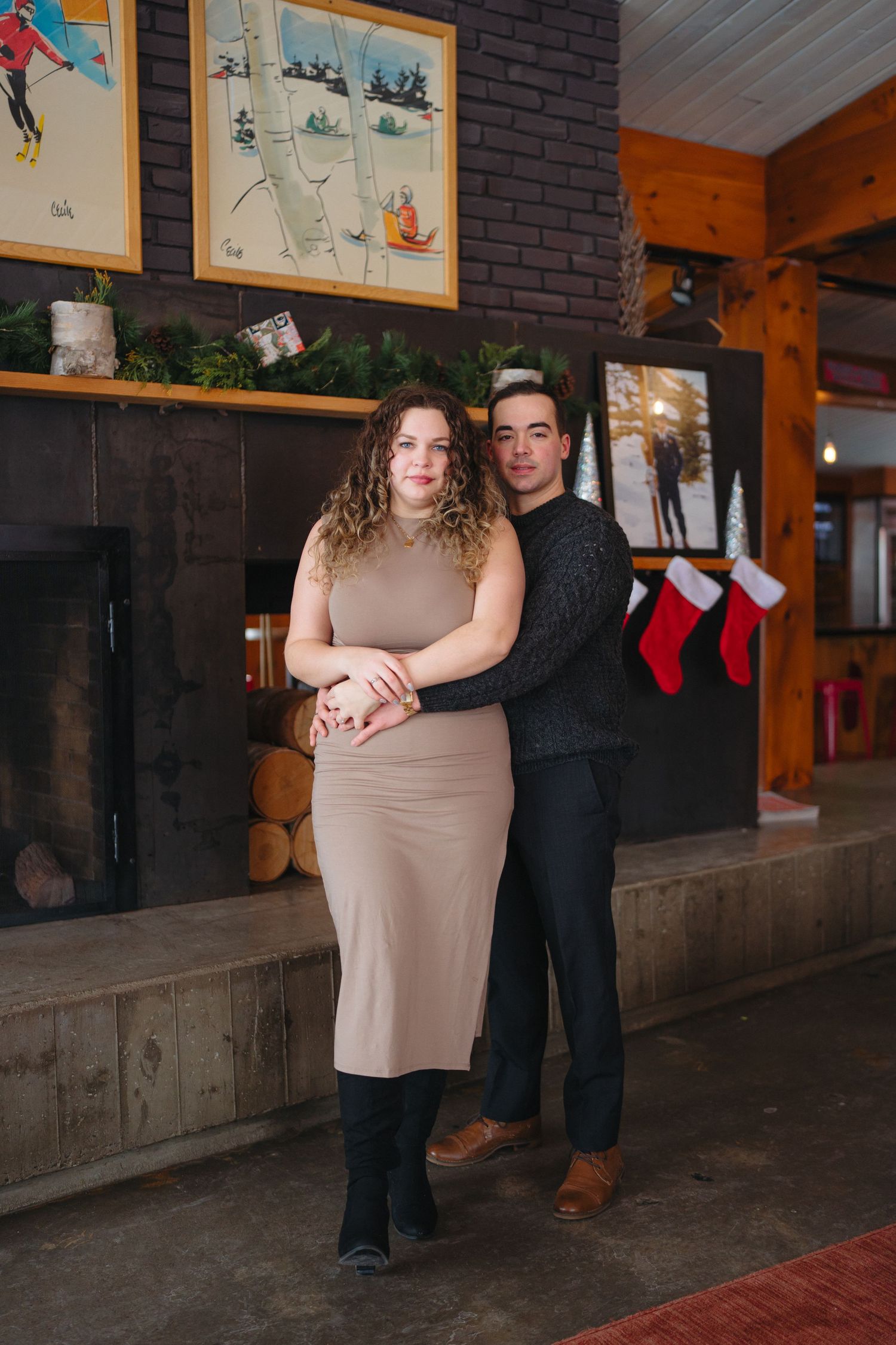 Romantic couple poses together in a rustic indoor setting with framed artwork on brick walls.