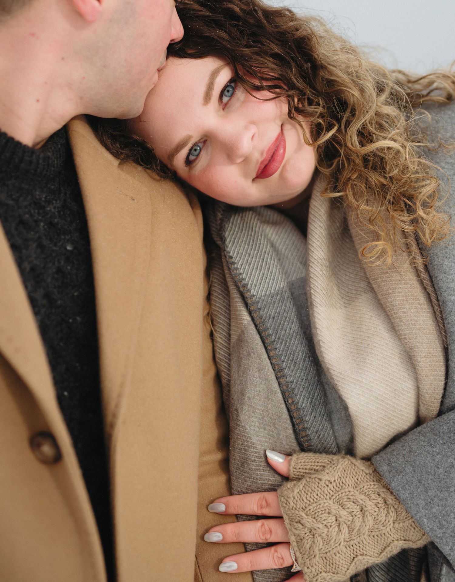 A romantic winter portrait of a couple in cozy neutral-toned coats with natural curly hair and warm styling.