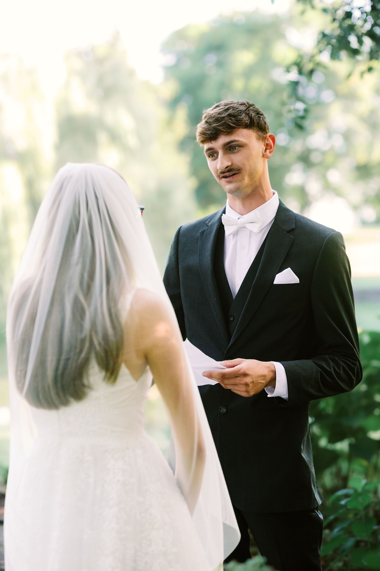 A couple exchanges vows during an outdoor wedding ceremony surrounded by lush greenery and natural light.