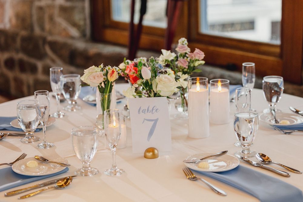 Elegant wedding reception tables set with blue and white decor, floral centerpieces, and glowing candles.