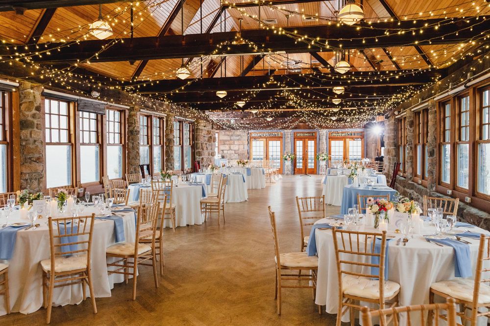 Wedding reception venue decorated with string lights and white linens features rustic wooden beams and elegant table settings.