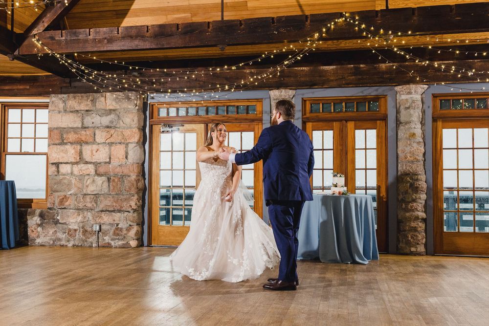 Rustic indoor wedding ceremony space with exposed stone walls and wooden beams decorated with string lights.
