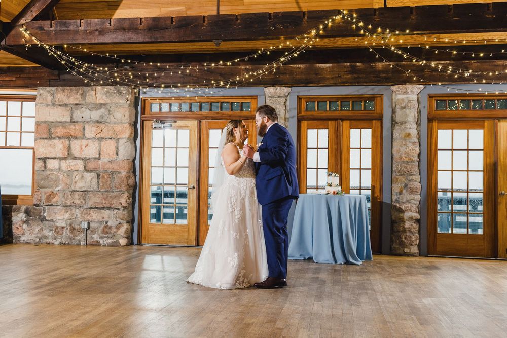 Rustic barn wedding venue interior decorated with twinkle lights and featuring exposed stone walls and hardwood floors.