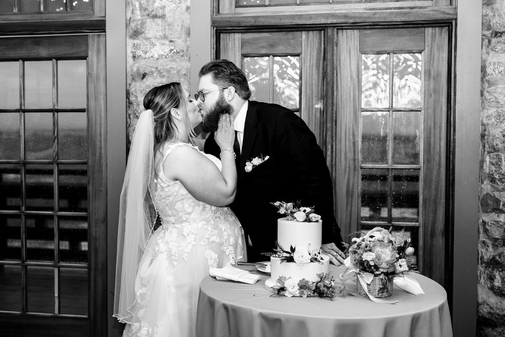 Black and white photo of couple sharing a moment by their wedding cake at reception.