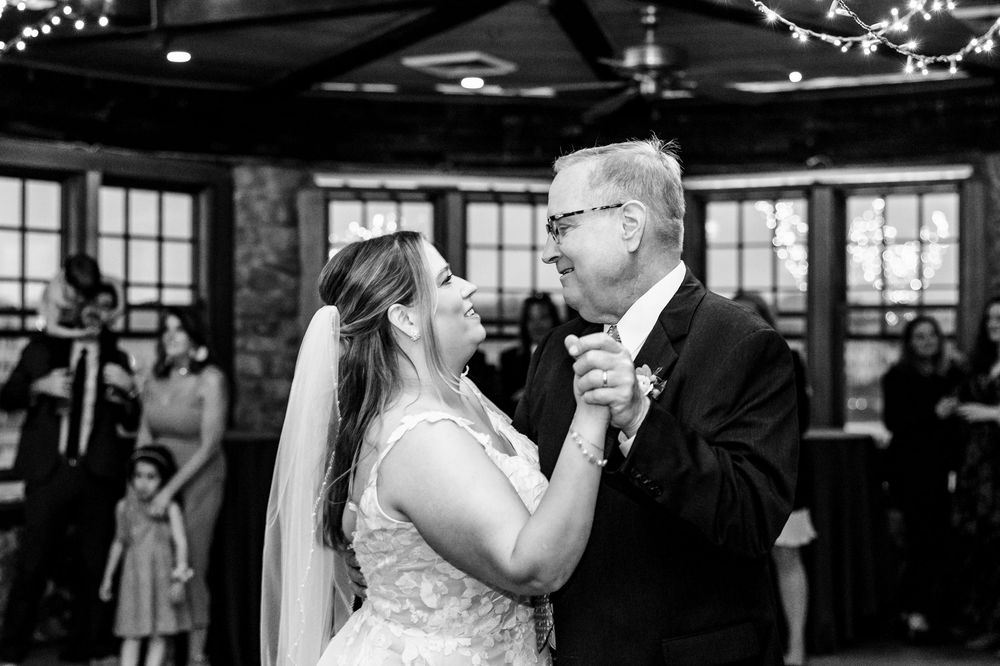 Black and white wedding reception photo showing couples dancing under twinkling lights in a romantic venue.