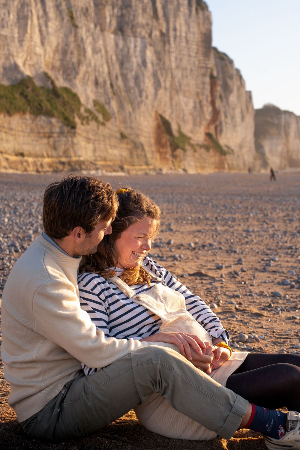 Happy couple sitting together on sandy beach with dramatic white cliffs in warm golden sunlight.