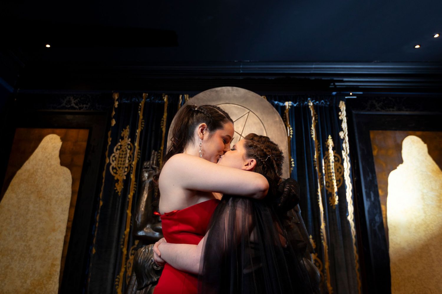 An alternative engaged couple kiss in front of the Baphomet statue at the Satanic Temple.
