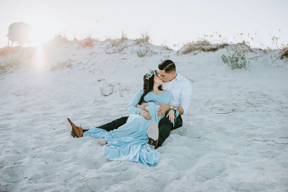 A sequence of playful movement shots showing someone rolling down a sandy beach slope in a blue dress.