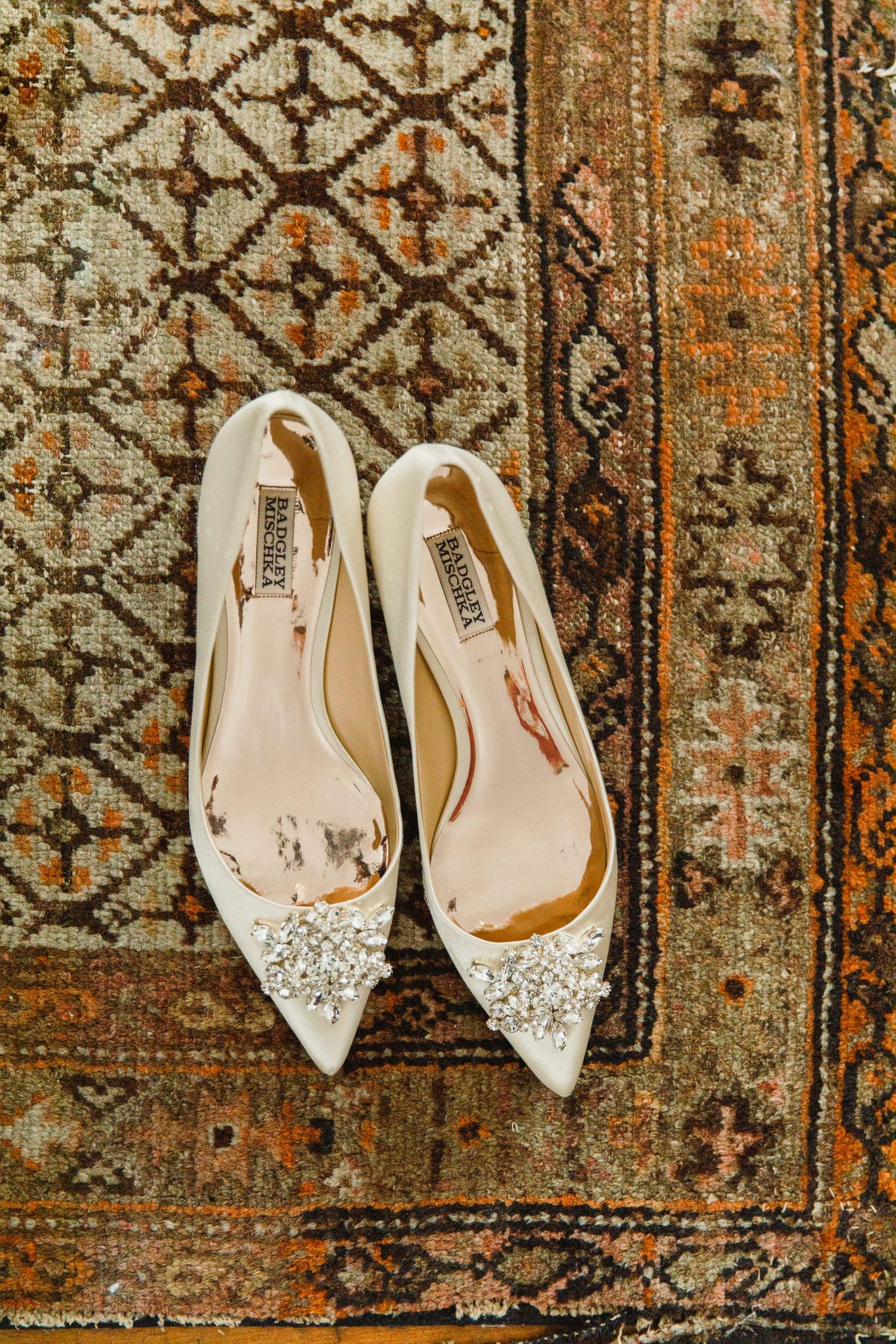 Elegant white crystal-embellished bridal shoes on a vintage patterned rug.