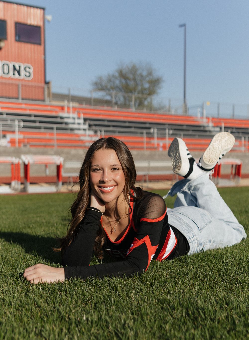 Student athlete in red and black uniform relaxes on sunny sports field during photo session.