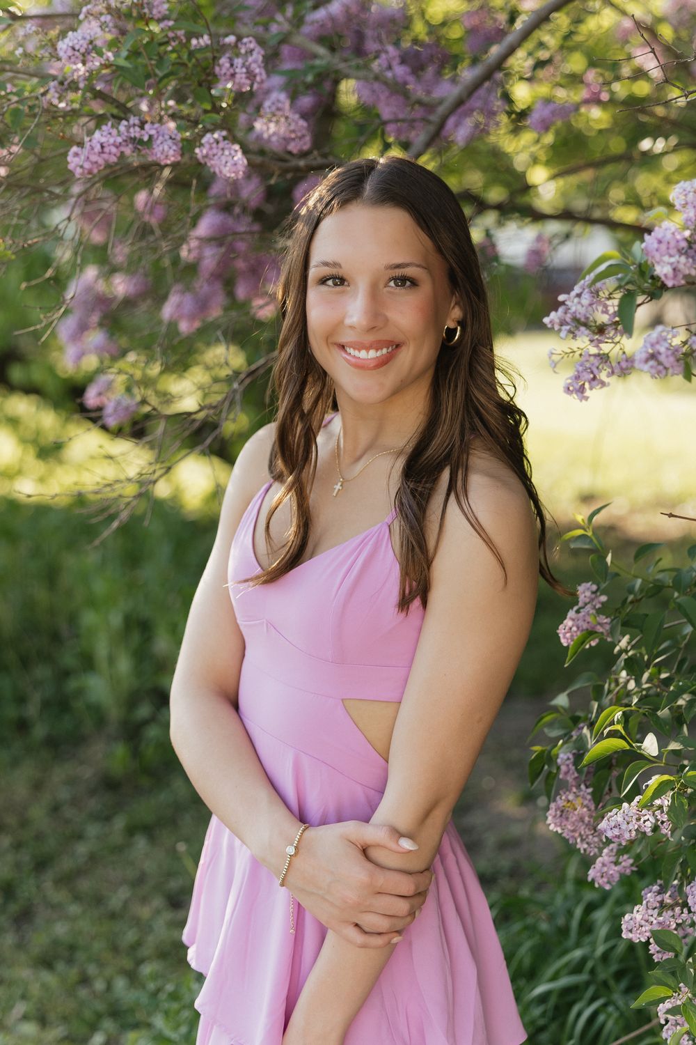 Spring portrait session in a garden with blooming lilac flowers and a pink sundress against golden sunlight.