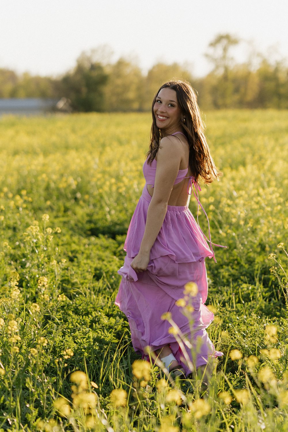 Young woman in flowing purple dress twirls through golden wildflower field at sunset.