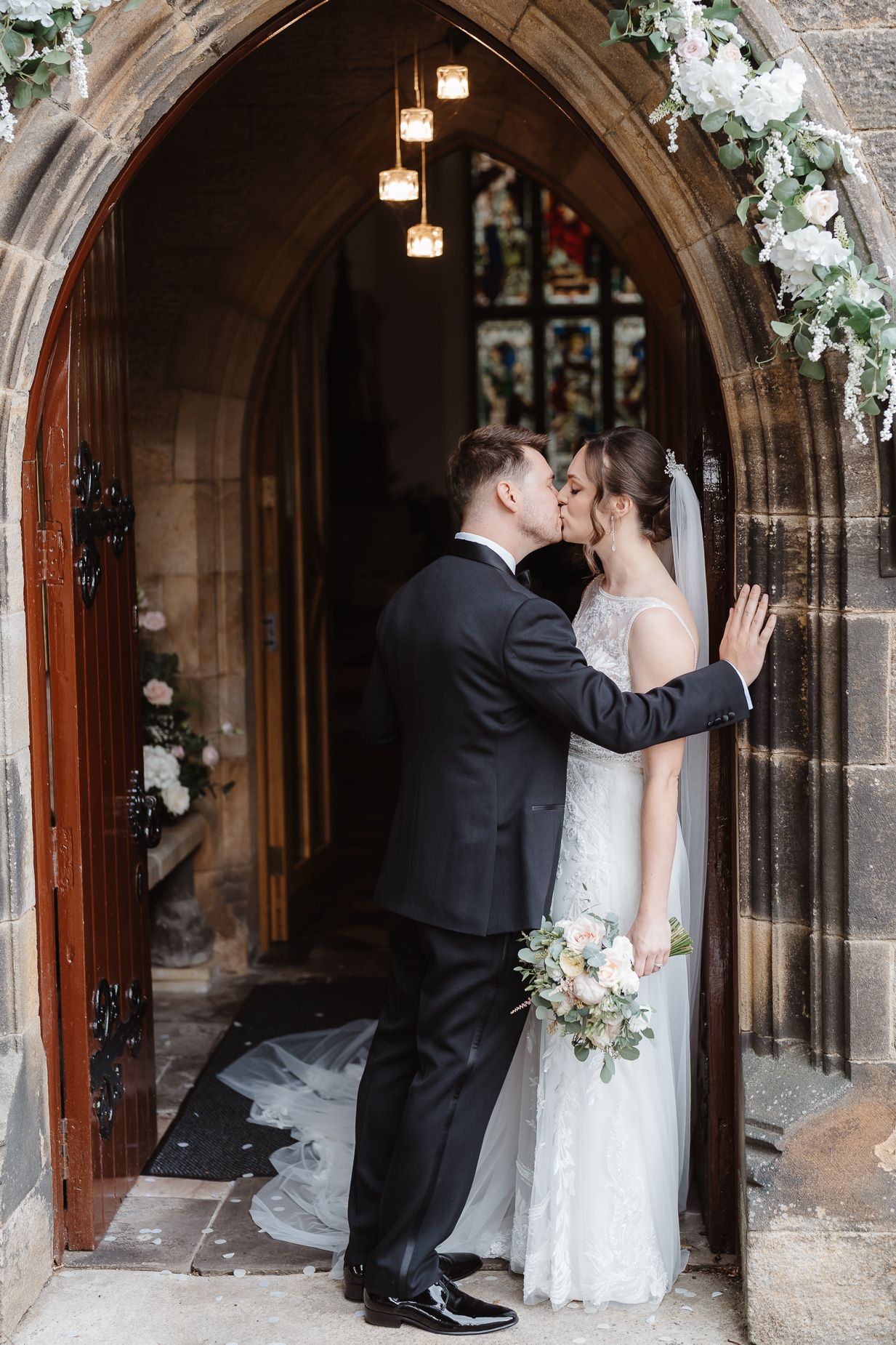 A romantic moment captured under a stone archway decorated with white floral arrangements.