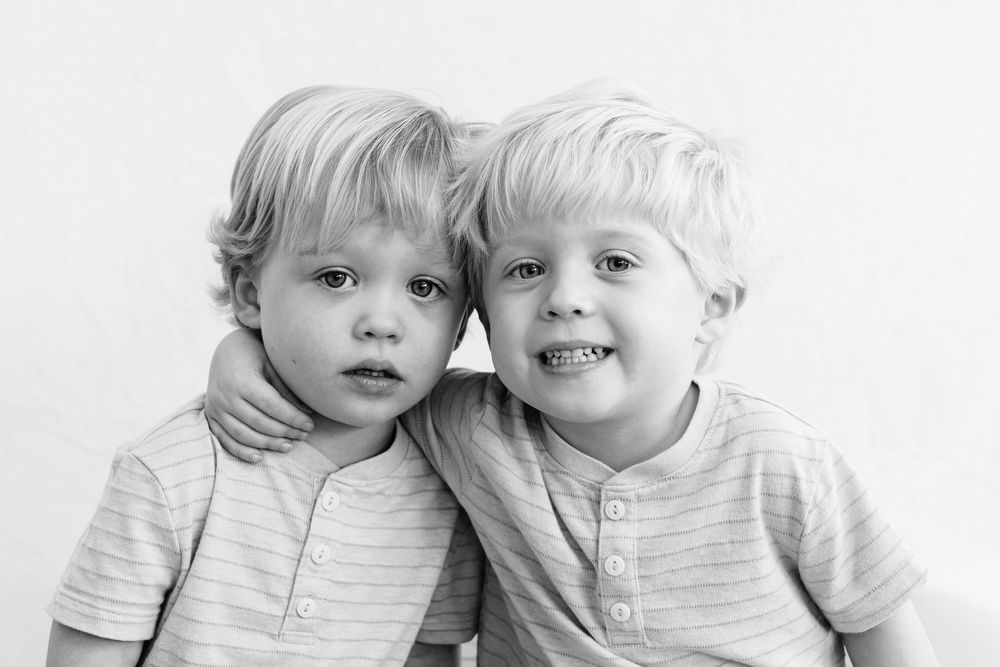 Two young children in light colored clothing sitting together and smiling at the camera.
