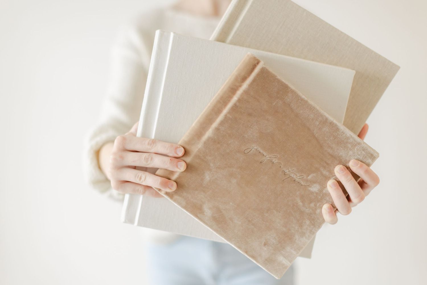 Hands in a white sweater holding vintage photo albums or scrapbooks against a light background.