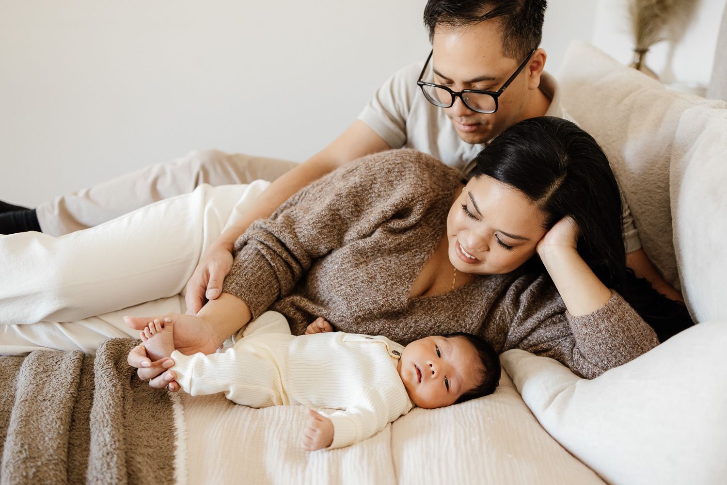 parents lay on their bed while their newborn baby looks into the camera