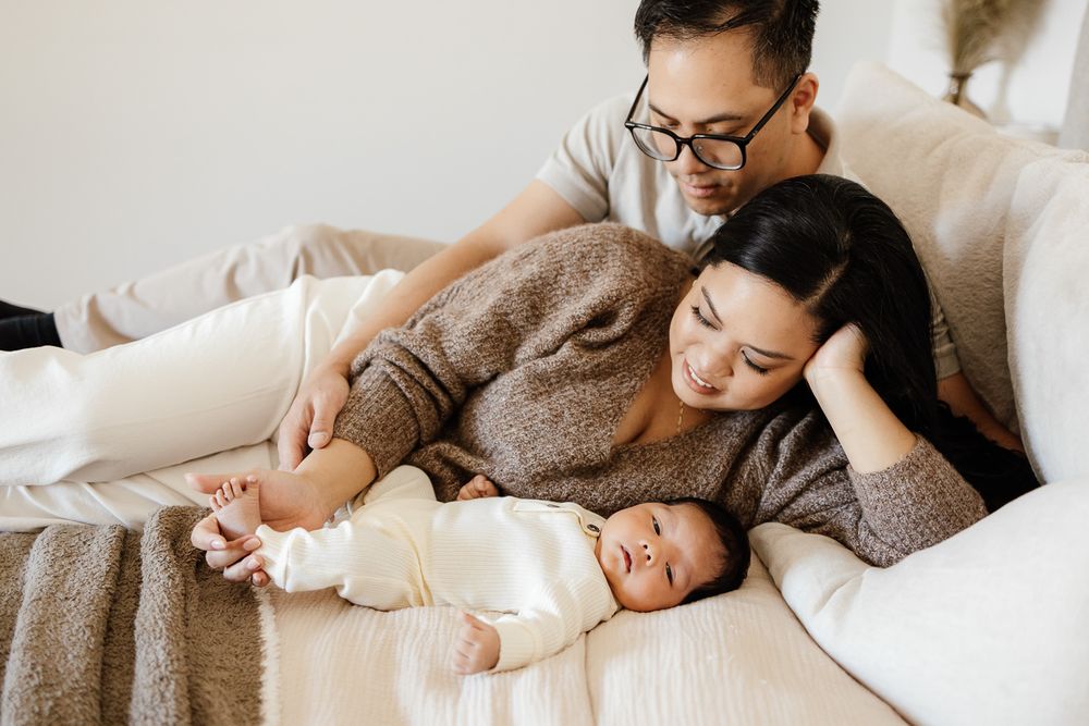 parents lay on their bed while their newborn baby looks into the camera